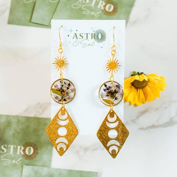 Bitter Dogbane – Moon Phases by Astro & Sol - Handcrafted brass crescent moon earrings featuring preserved purple dogbane flowers encased within the celestial frames.