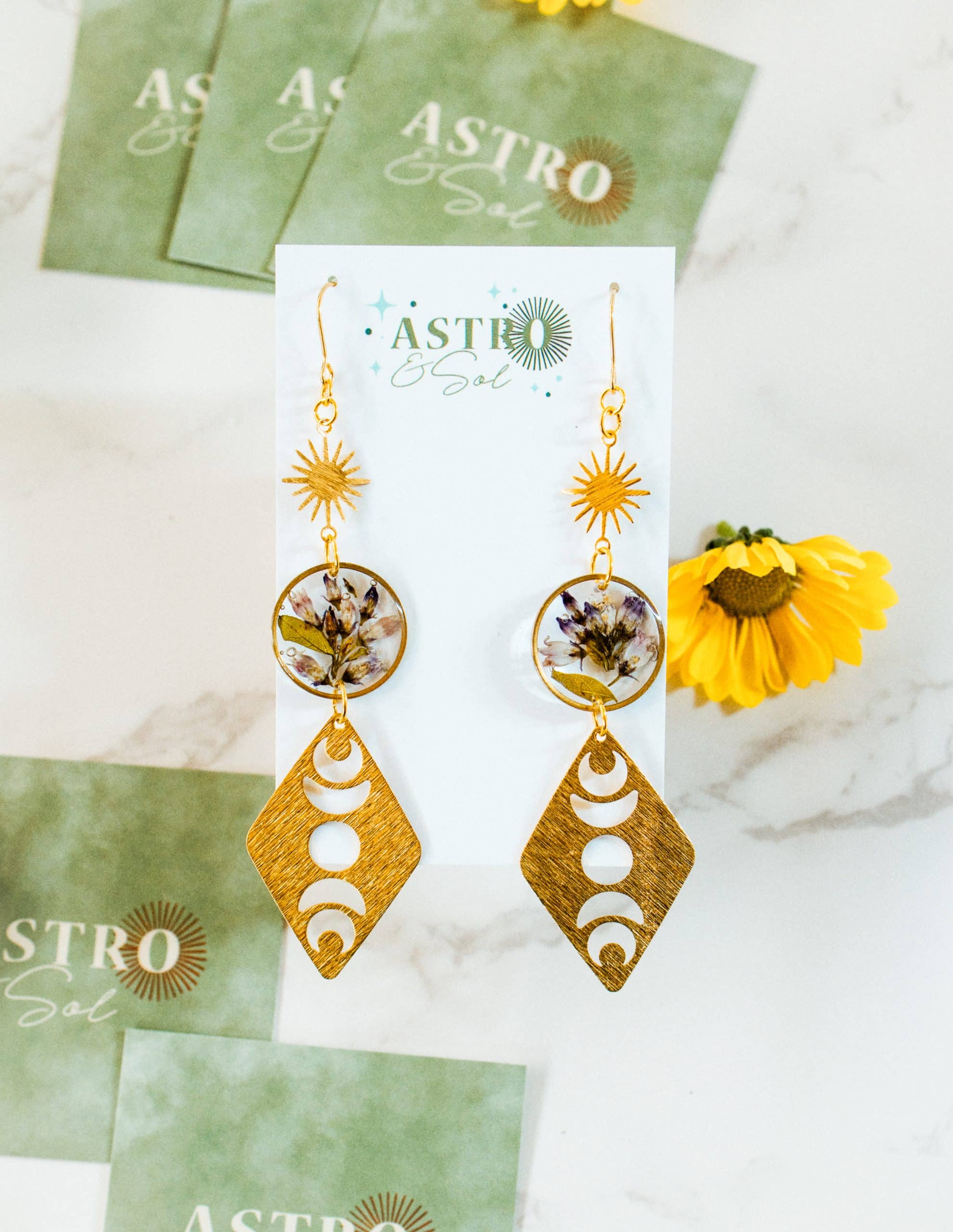 Bitter Dogbane – Moon Phases by Astro & Sol - Handcrafted brass crescent moon earrings featuring preserved purple dogbane flowers encased within the celestial frames.